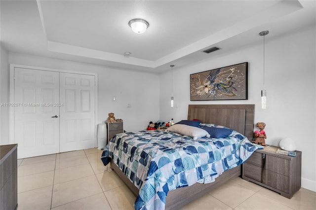 tiled bedroom with a tray ceiling and a closet