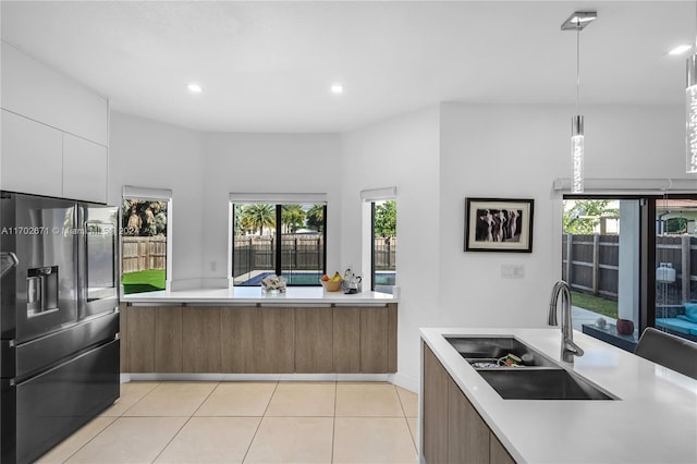 kitchen featuring pendant lighting, sink, stainless steel fridge with ice dispenser, plenty of natural light, and white cabinetry