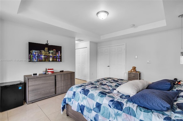 bedroom featuring light tile patterned flooring, black fridge, and a tray ceiling