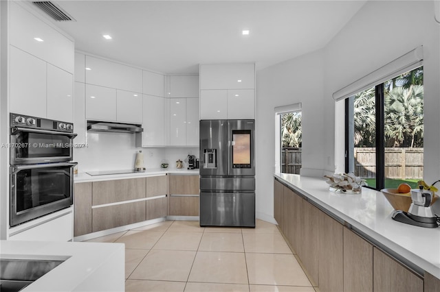 kitchen featuring white cabinets, light tile patterned floors, light brown cabinetry, and appliances with stainless steel finishes