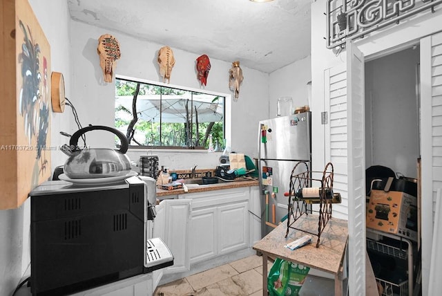 kitchen featuring stainless steel refrigerator, sink, and white cabinets