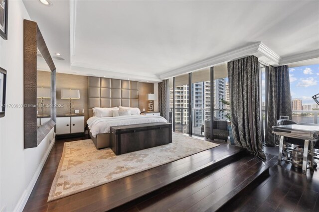 bedroom with ornamental molding, a tray ceiling, expansive windows, and dark wood-type flooring