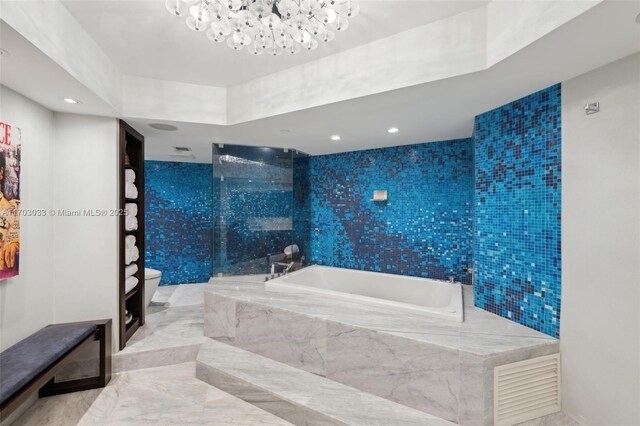 bathroom featuring an inviting chandelier, tiled bath, and toilet