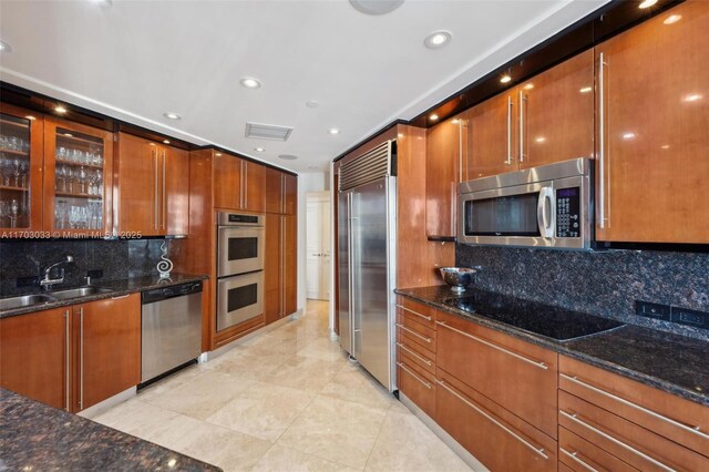 kitchen featuring decorative backsplash, appliances with stainless steel finishes, dark stone counters, and sink