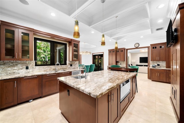 kitchen featuring sink, beamed ceiling, an island with sink, pendant lighting, and decorative backsplash