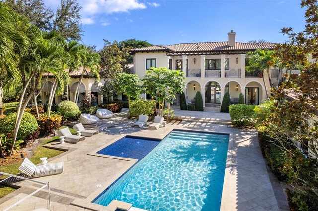 5935 Moss Ranch Rd, Pinecrest, FL 33156 - back of house with a chimney, a patio, a balcony, an outdoor pool, and stucco siding