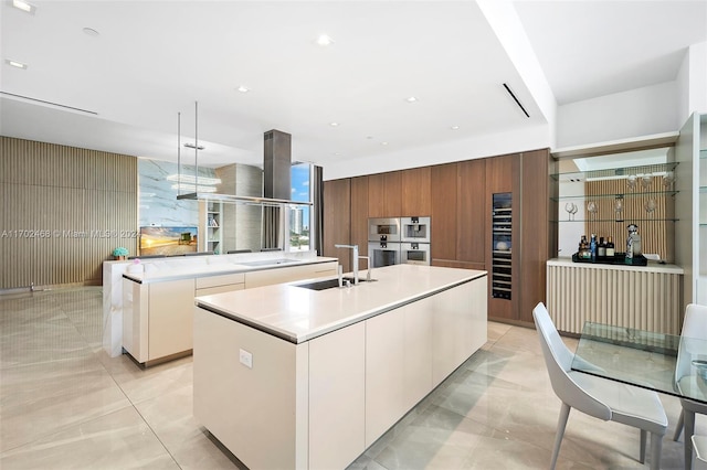 kitchen featuring pendant lighting, a kitchen island with sink, sink, double oven, and white cabinetry