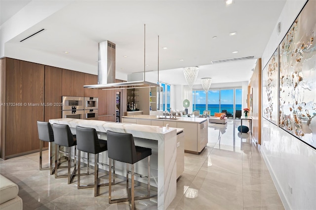 kitchen with a spacious island, light countertops, hanging light fixtures, a sink, and island range hood