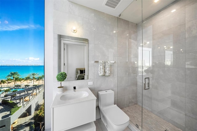 bathroom with toilet, a water view, vanity, a shower with shower door, and tile walls