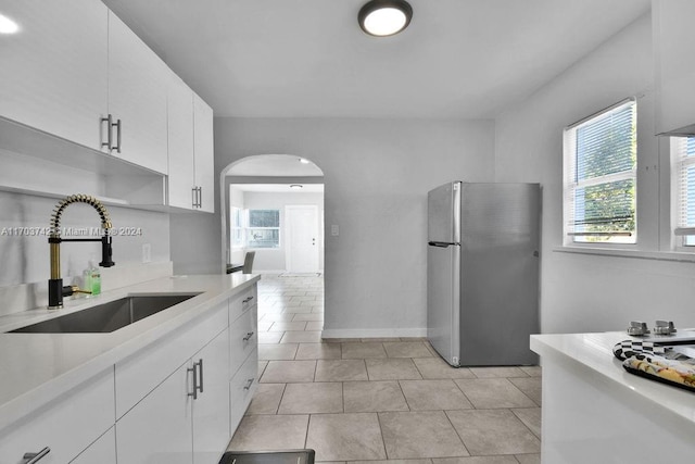 kitchen featuring light tile patterned flooring, stainless steel fridge, white cabinetry, and sink