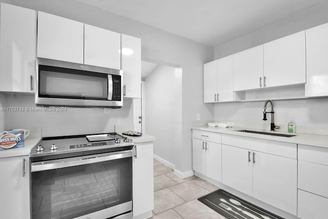 kitchen with appliances with stainless steel finishes, light tile patterned floors, white cabinetry, and sink