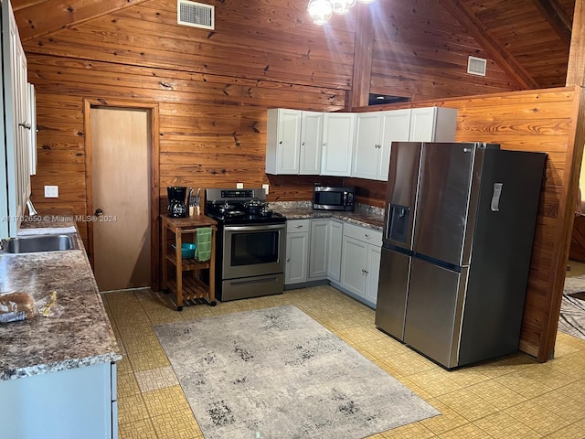 kitchen featuring wood walls, wooden ceiling, dark stone counters, appliances with stainless steel finishes, and beamed ceiling