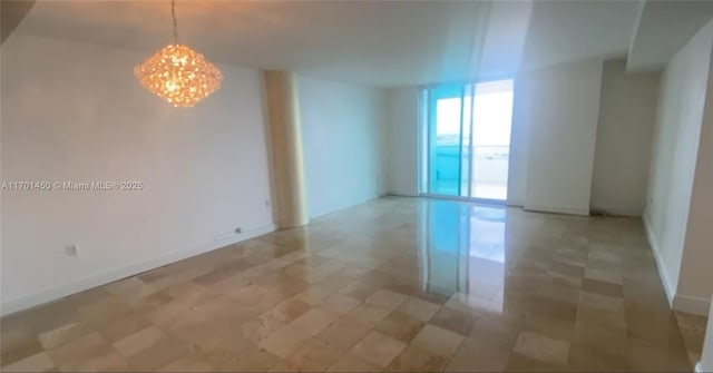 unfurnished room featuring a chandelier, baseboards, and a wall of windows