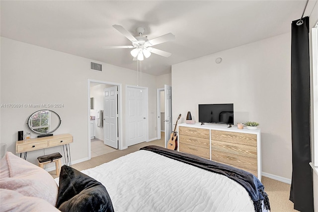 bedroom with ceiling fan, light colored carpet, and ensuite bathroom