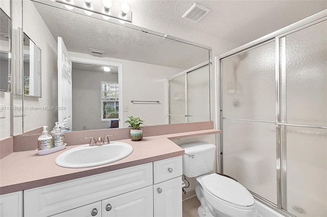 bathroom with vanity, toilet, an enclosed shower, and a textured ceiling