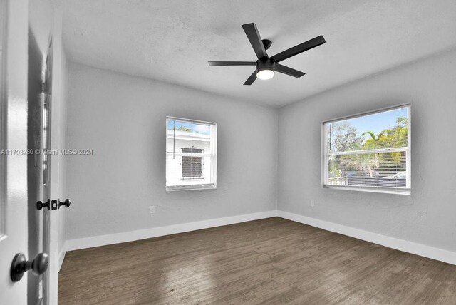 empty room featuring ceiling fan, a healthy amount of sunlight, and dark hardwood / wood-style flooring