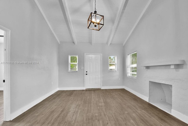 unfurnished living room with lofted ceiling with beams, dark hardwood / wood-style floors, a brick fireplace, and a wealth of natural light