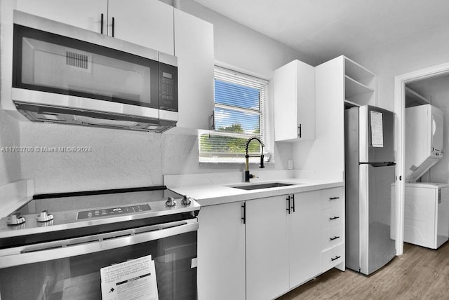 kitchen with stacked washer and clothes dryer, white cabinets, sink, light wood-type flooring, and appliances with stainless steel finishes