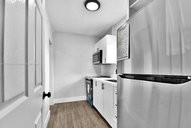 kitchen with white cabinets, appliances with stainless steel finishes, and light hardwood / wood-style flooring