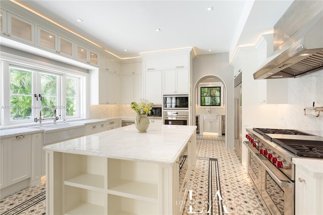 kitchen featuring a center island, wall chimney range hood, tasteful backsplash, white cabinetry, and stainless steel appliances