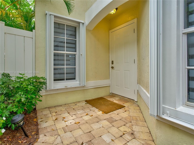 view of exterior entry featuring fence and stucco siding