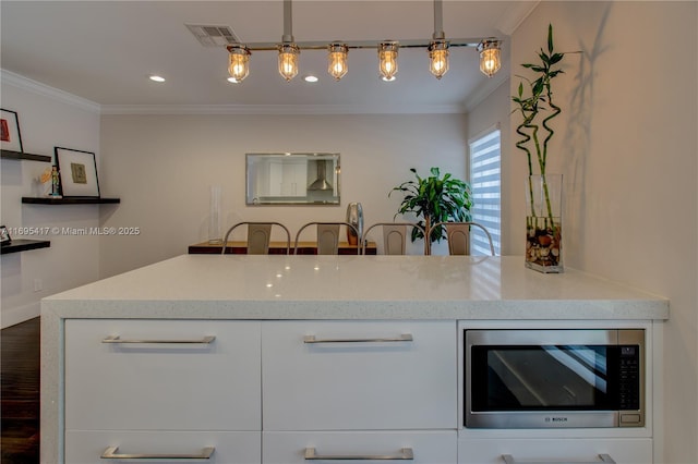 kitchen featuring visible vents, stainless steel microwave, white cabinets, and crown molding