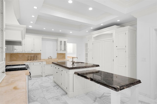 kitchen with decorative backsplash, white cabinetry, a breakfast bar, and an island with sink