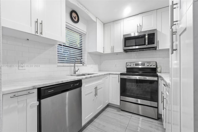 kitchen featuring backsplash, sink, appliances with stainless steel finishes, light stone counters, and white cabinetry