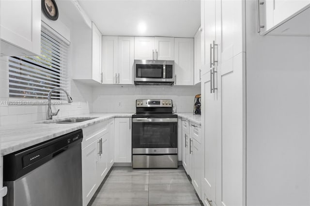 kitchen with light stone countertops, sink, white cabinetry, and stainless steel appliances