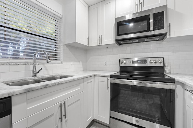 kitchen with stainless steel appliances, white cabinetry, a sink, and light stone counters