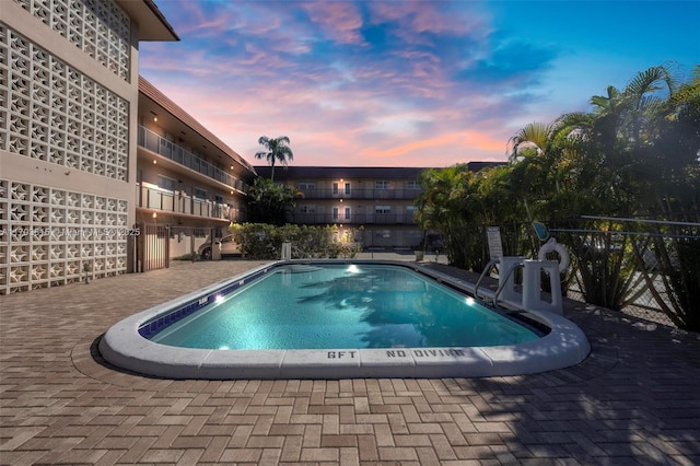 pool at dusk with a patio area, fence, and a community pool