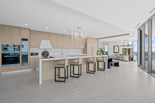 kitchen featuring light brown cabinetry, hanging light fixtures, a large island, backsplash, and an inviting chandelier