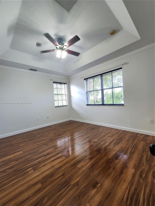 empty room with dark wood-type flooring, a raised ceiling, crown molding, ceiling fan, and a textured ceiling