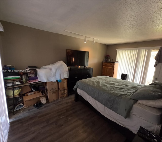 bedroom featuring track lighting, dark wood-type flooring, and a textured ceiling