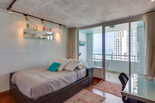 bedroom featuring a water view, wood-type flooring, rail lighting, and access to outside