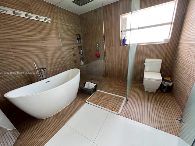 bathroom featuring plus walk in shower, tile patterned floors, tile walls, and toilet