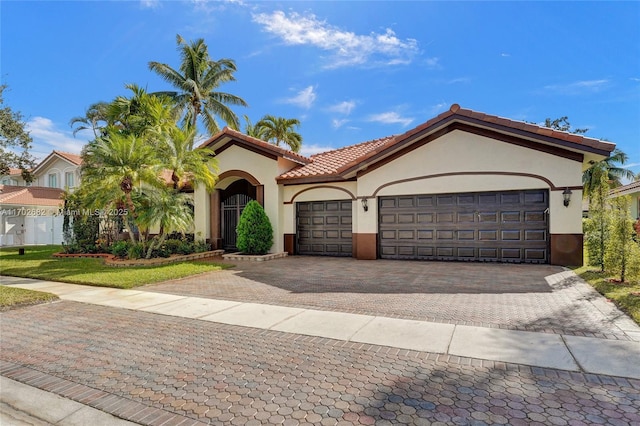 mediterranean / spanish-style house featuring a tiled roof, decorative driveway, an attached garage, and stucco siding