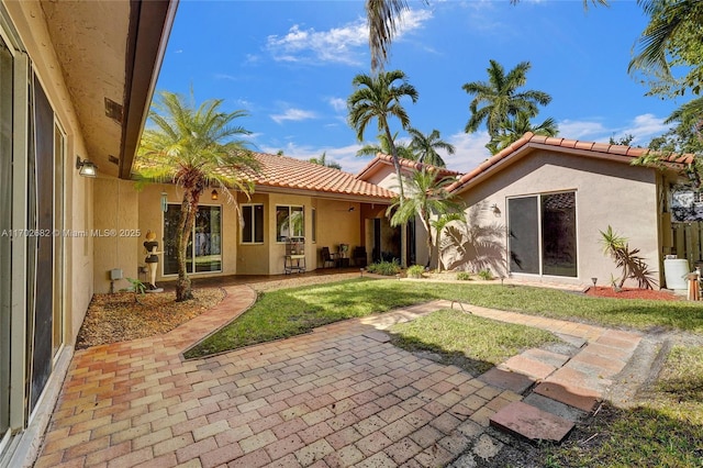 rear view of property featuring stucco siding, a yard, a tile roof, and a patio area