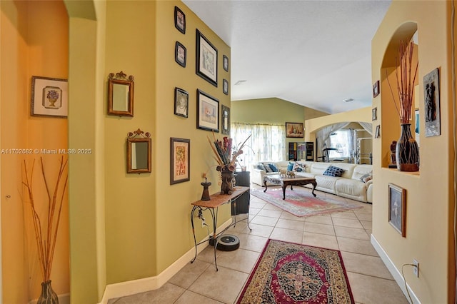 corridor featuring light tile patterned floors, baseboards, arched walkways, and vaulted ceiling