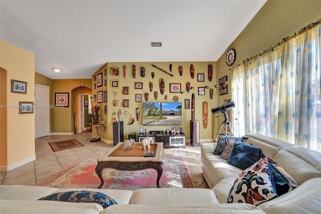 living room with light tile patterned floors, visible vents, baseboards, arched walkways, and vaulted ceiling