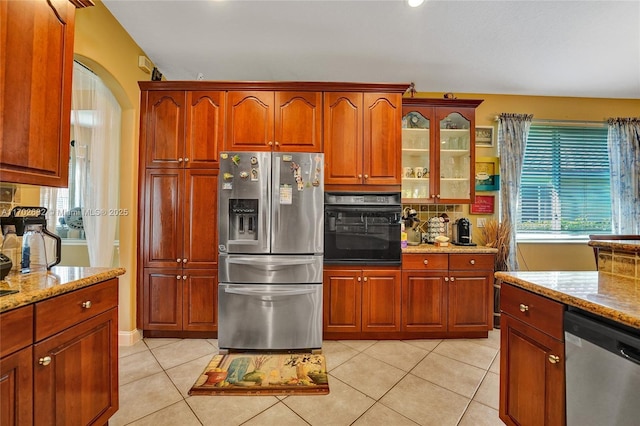 kitchen featuring glass insert cabinets, light stone countertops, light tile patterned floors, arched walkways, and stainless steel appliances