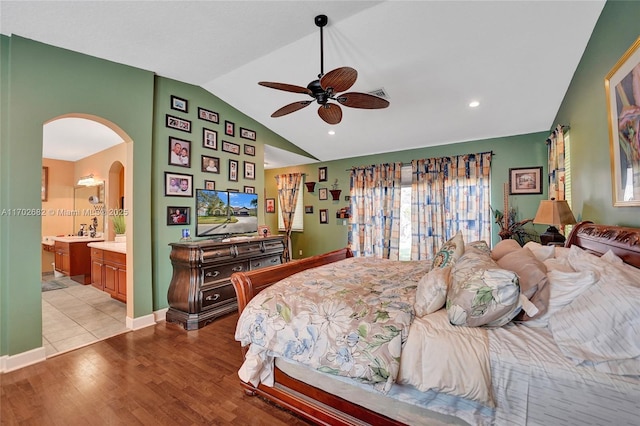 bedroom featuring baseboards, vaulted ceiling, light wood-style flooring, arched walkways, and ensuite bath