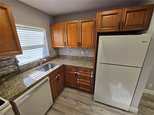 kitchen featuring backsplash, dark stone counters, white appliances, sink, and light hardwood / wood-style flooring