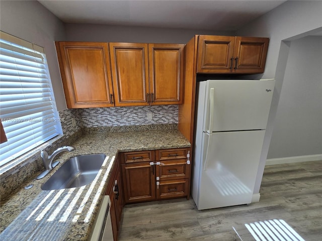 kitchen featuring light stone countertops, backsplash, sink, white refrigerator, and hardwood / wood-style flooring