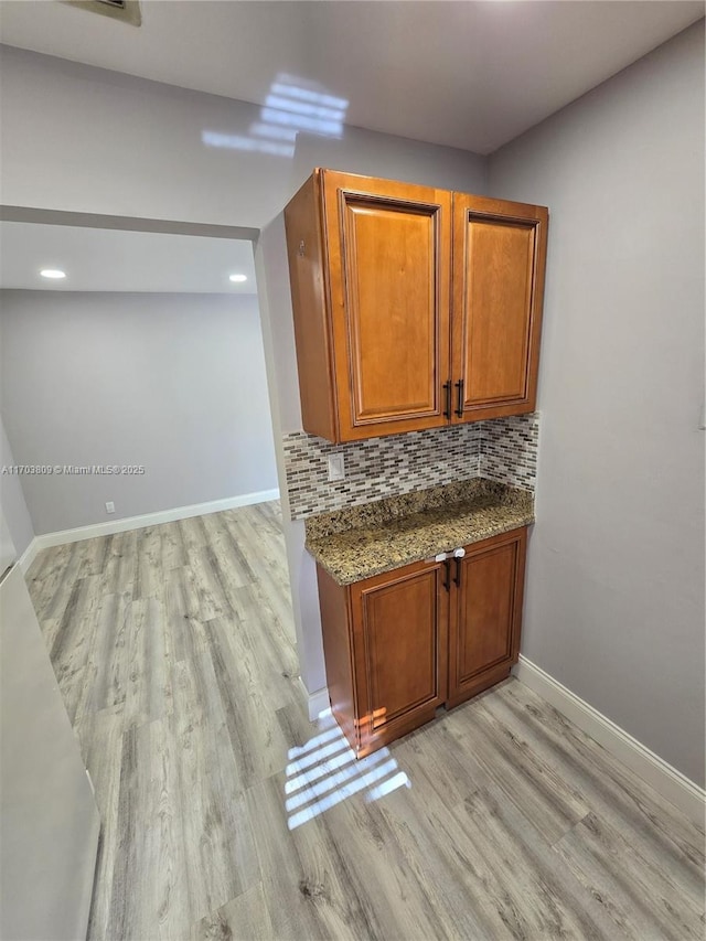 bar with backsplash, dark stone countertops, and light hardwood / wood-style floors