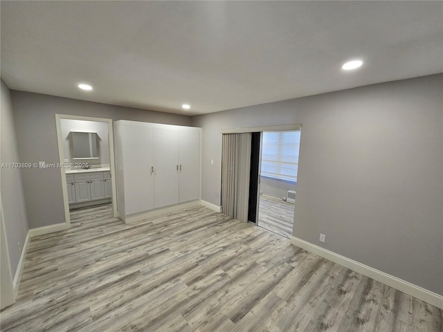 unfurnished bedroom with ensuite bathroom, light wood-type flooring, and a closet