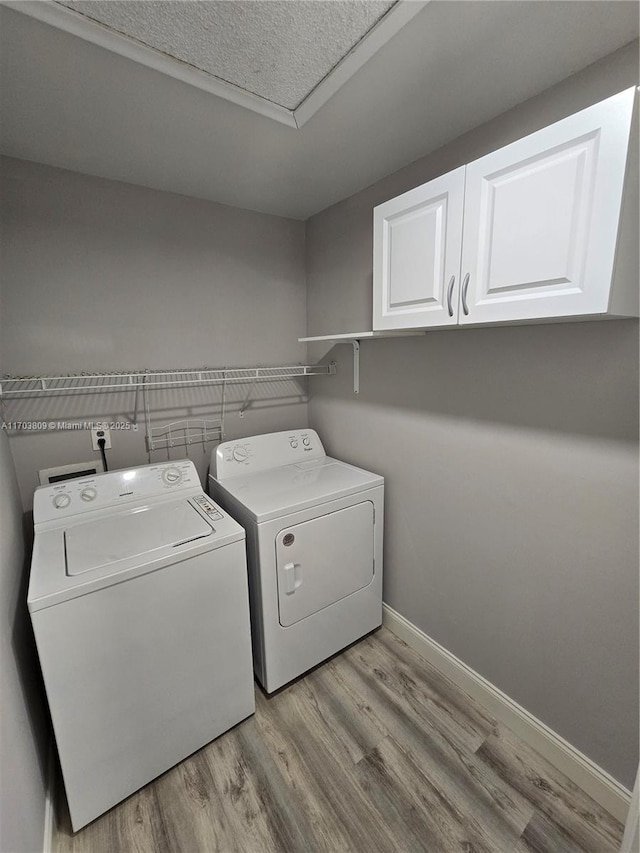 clothes washing area with washer and dryer, cabinets, and light hardwood / wood-style flooring