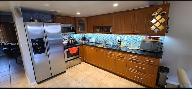 kitchen with backsplash, stainless steel appliances, sink, light tile patterned floors, and dark stone countertops