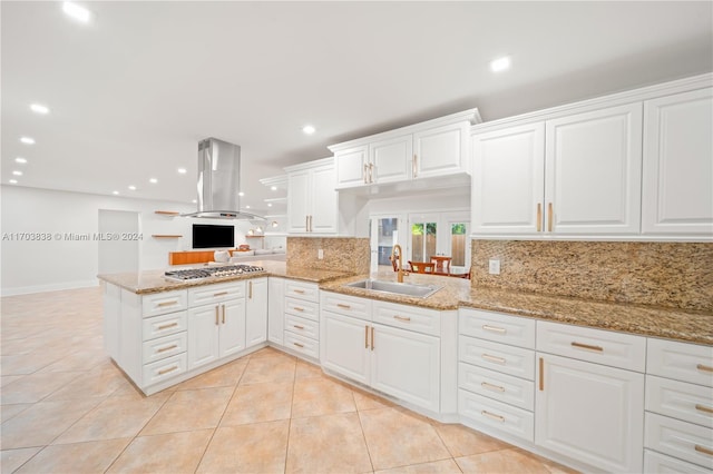 kitchen featuring stainless steel gas stovetop, white cabinets, sink, island range hood, and kitchen peninsula