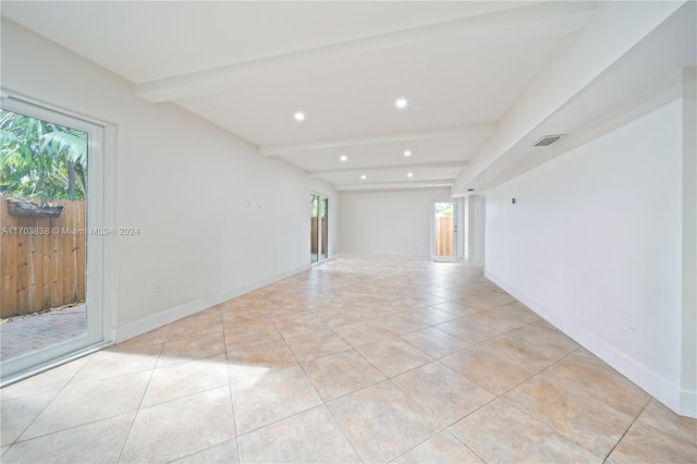 tiled spare room featuring plenty of natural light and beamed ceiling